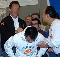 With a little help from Chinese weightlifting coach Chen Wenbin, California Governor Arnold Schwarzenegger autographs Zhang Guozheng's sweatshirt. IronMind® | Randall J. Strossen, Ph.D. photo.