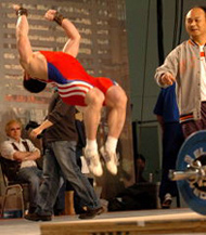 Shi Zhiyong (China) capped off his performance with a back flip, as coach Chen Wenbin looks on. IronMind® | Randall J. Strossen, Ph.D. photo.